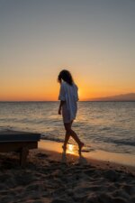 A woman strolls along Thasos' beach during a breathtaking sunset, capturing the essence of relaxation and summer.