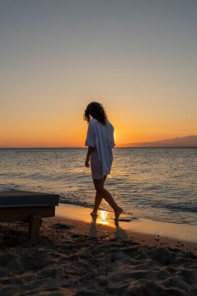 A woman strolls along Thasos' beach during a breathtaking sunset, capturing the essence of relaxation and summer.