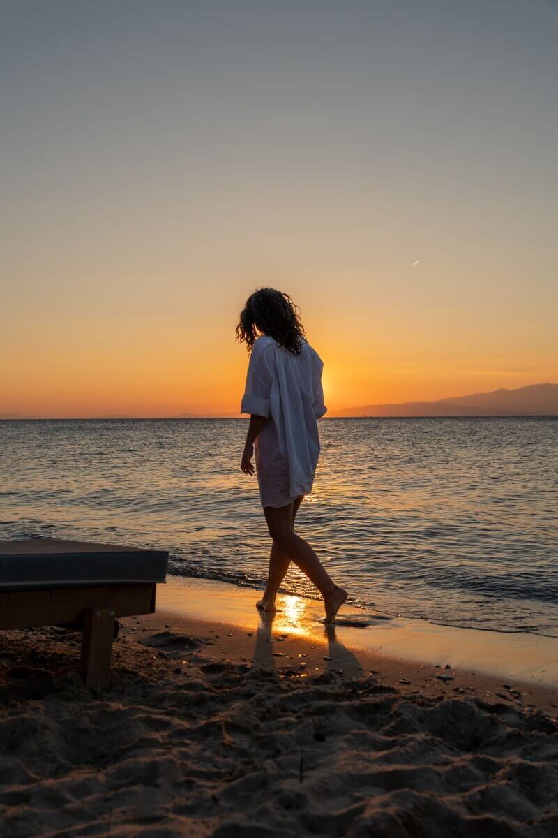 A woman strolls along Thasos' beach during a breathtaking sunset, capturing the essence of relaxation and summer.