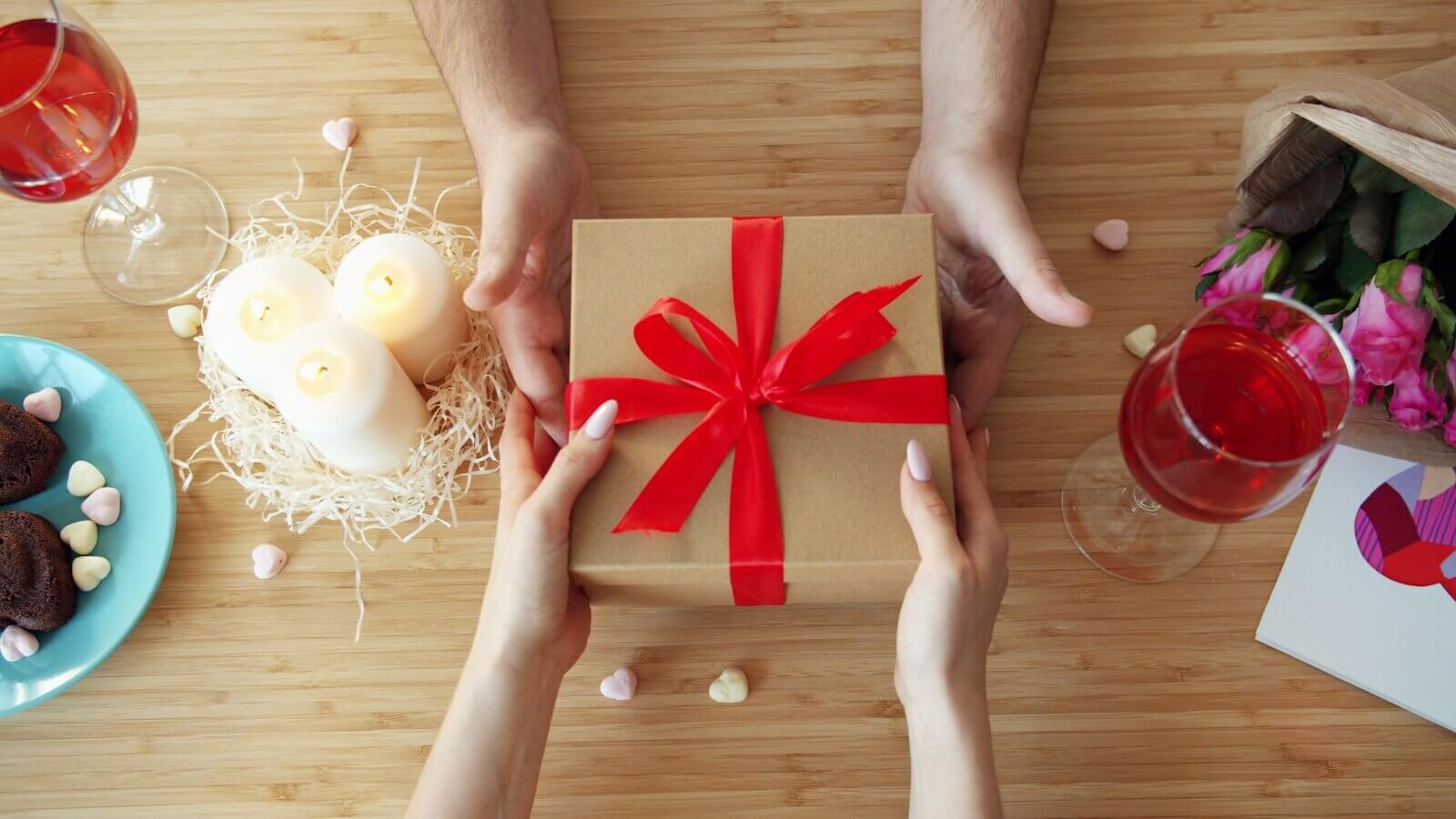 Hands exchanging a gift with red ribbon.