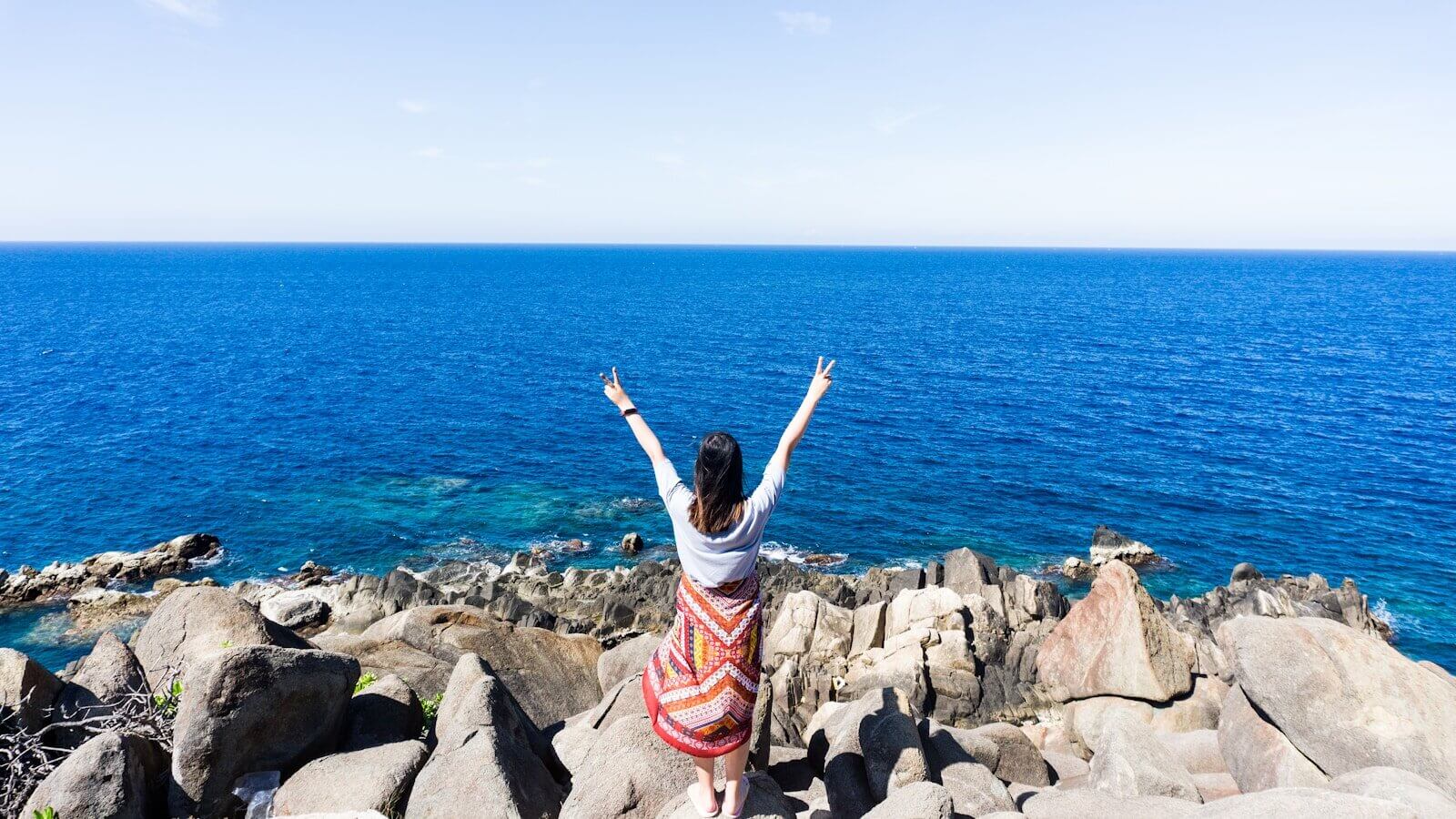 woman in white and red dress standing on rocky shore during daytime