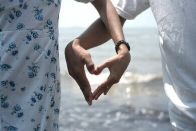 Couple forms heart shape with hands at beach.